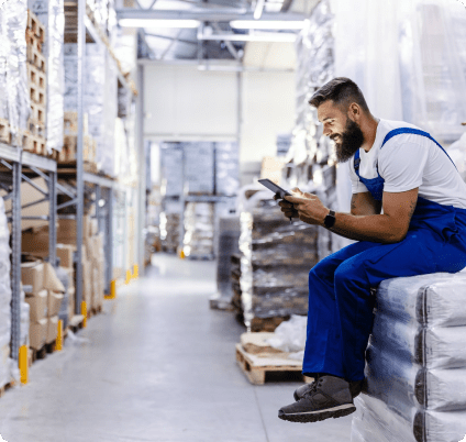 Man hunched over, sitting on top of overstock inventory looking into his mobile phone.